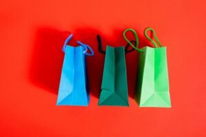 Three colorful paper shopping bags on a striking red backdrop, ideal for shopping and sale themes.