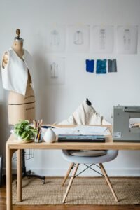 A stylish sewing studio featuring a mannequin, sewing machine, sketches, and fabric swatches on a wooden table.