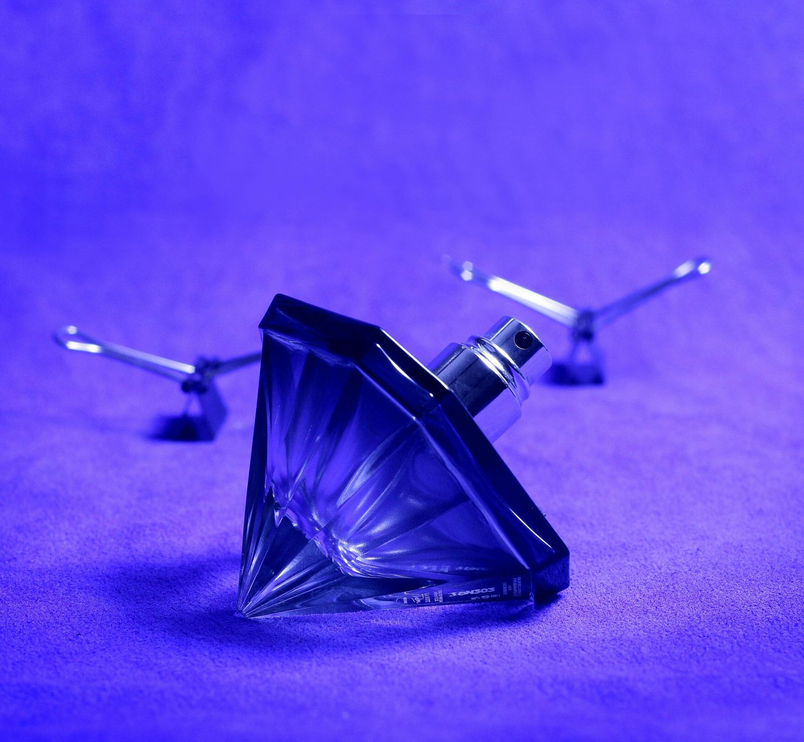 A stylish still life featuring a diamond-shaped perfume bottle against a blue background.